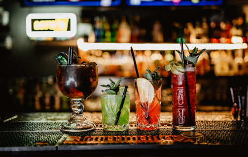 Rozmaite kolorowe drinki ustawione w linii na barze.